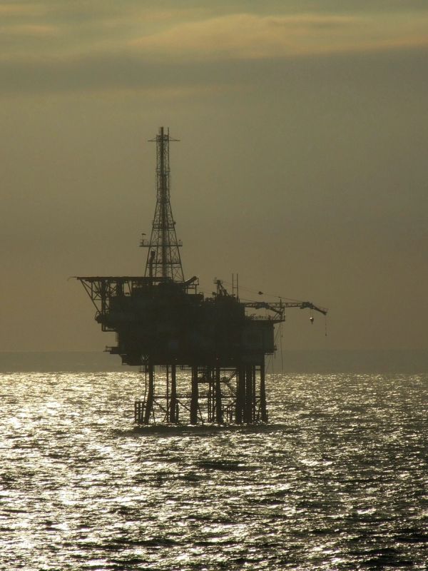 Silhouette of an offshore oil platform against the shimmering sea at dusk.