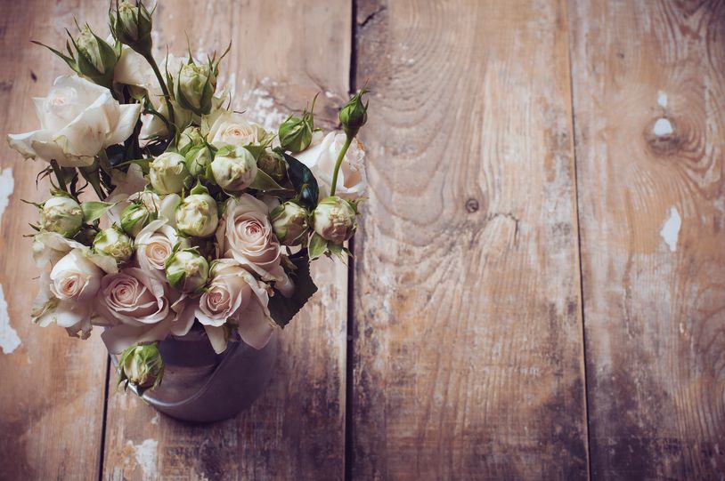 A bouquet of white roses in a vase on a rustic wooden table.