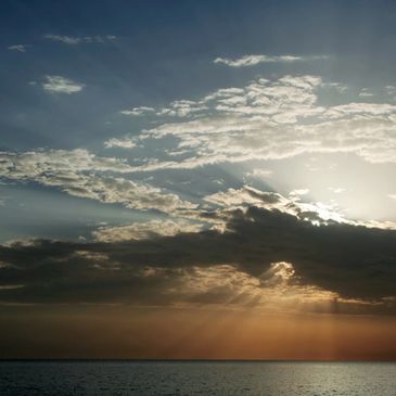 Sunset over the ocean with rays breaking through clouds.