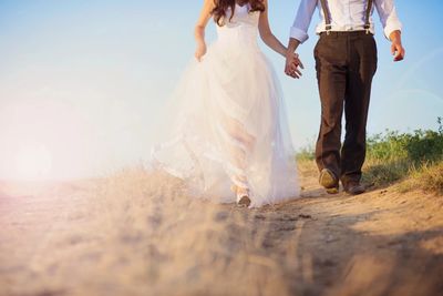 Couple holding hands walking outdoors, bride in a white dress.