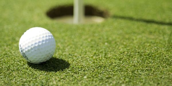 A golf ball on the green near the hole, ready to be putted.