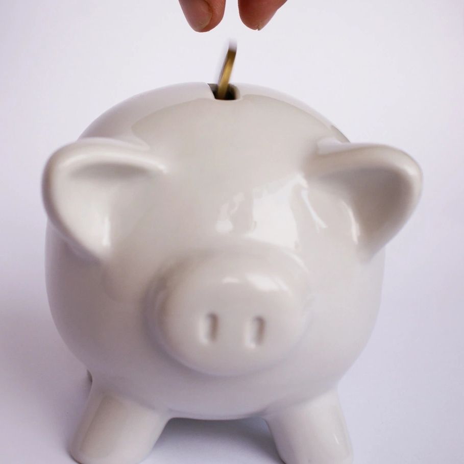 Hand putting coin in white piggy bank.