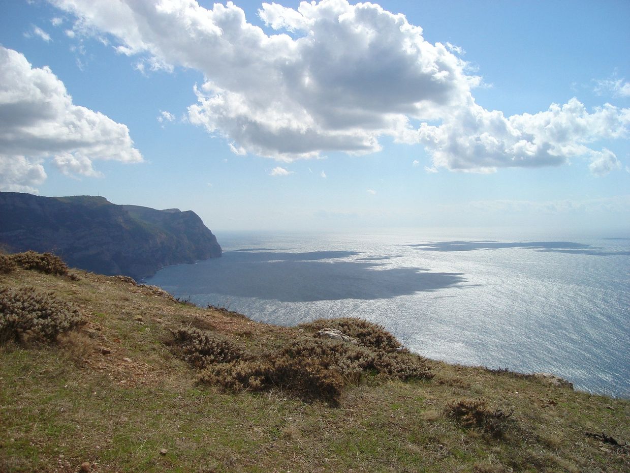 Coastal cliff overlooking a calm sea with fluffy clouds above.