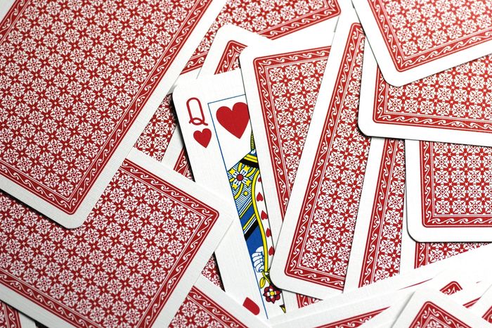A queen of hearts card peeks out from a scattered pile of red-backed playing cards.