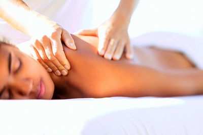 A young woman lying with her eyes closed. She is being massaged on her shoulder.