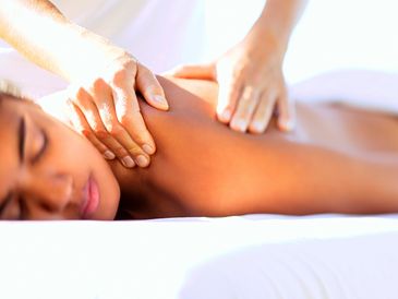 Dark woman laying down on a white table as hands massage her shoulder and back