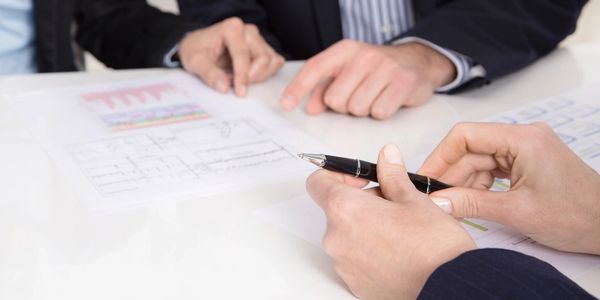 Close up image of hands holdig pen in front of other hands pointing at paperwork