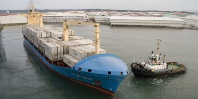 A large container ship guided by a tugboat near the port.