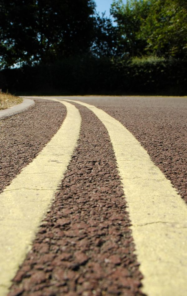Close-up of a curved road with double yellow lines and trees in the background.