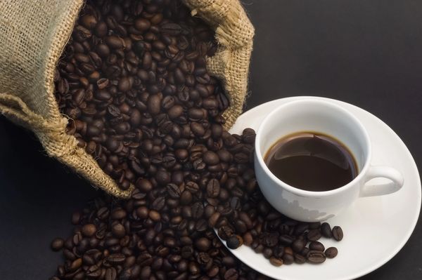 Coffee beans spilling from sack beside a cup of coffee.