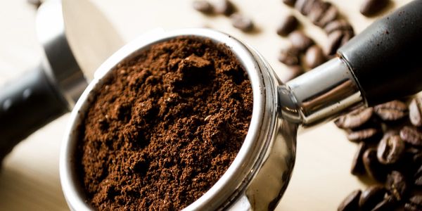 Close-up of ground coffee in a portafilter with coffee beans scattered around.