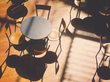 Empty round table with chairs casting shadows in sunlight.