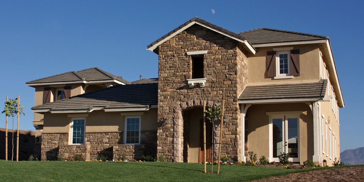 Modern suburban house with stone and stucco exterior under a clear blue sky.