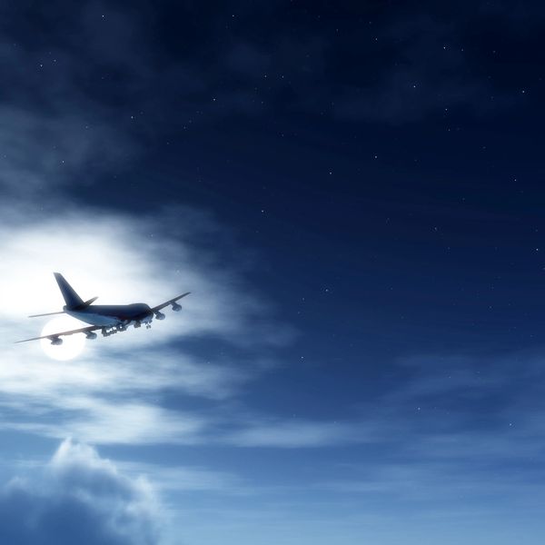 Airplane flying through a night sky illuminated by the moon.