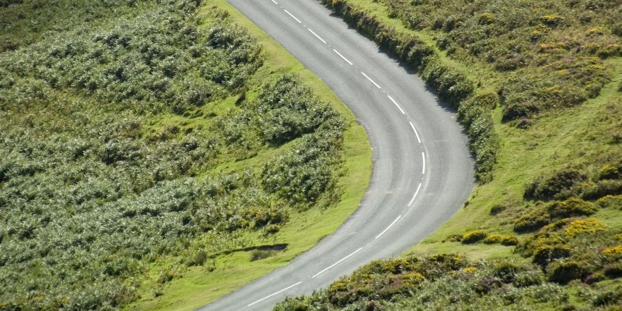 Curving road through lush green countryside with dense vegetation.
