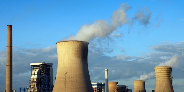 Industrial cooling towers releasing steam under a clear blue sky.