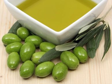 Fresh green olives next to a bowl of olive oil and olive leaves.