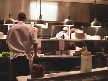 Chefs preparing food in a busy restaurant kitchen with warm lighting.