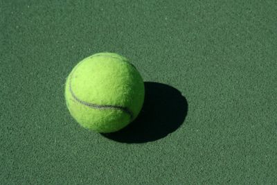 A tennis ball casting a shadow on a green court.