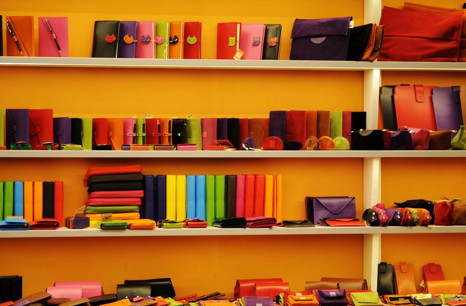 Colorful leather wallets and accessories neatly displayed on shelves against an orange wall.