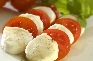 Sliced mozzarella and tomato with black pepper, garnished with basil.