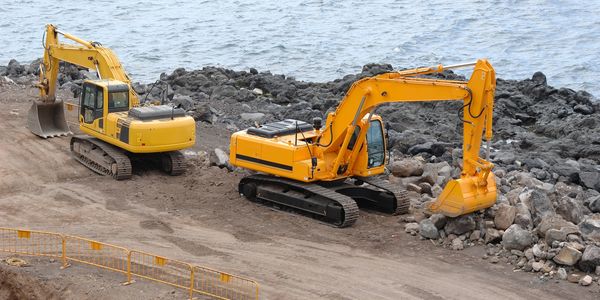 In the construction site, two excavators are working together to clean up large rocks from the area.