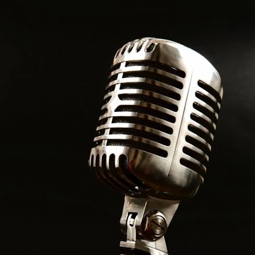 A vintage silver microphone against a black background.