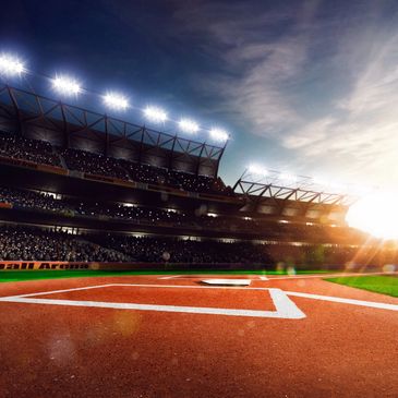 Sunlit baseball stadium with empty home plate and glowing floodlights.