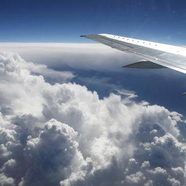 View of airplane wing above fluffy clouds.