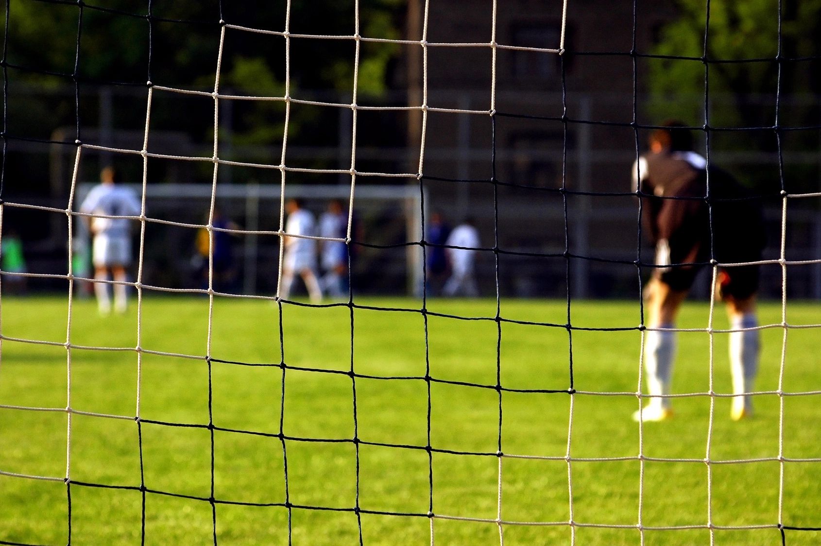 Visual of soccer field through the goalkeeper's net.