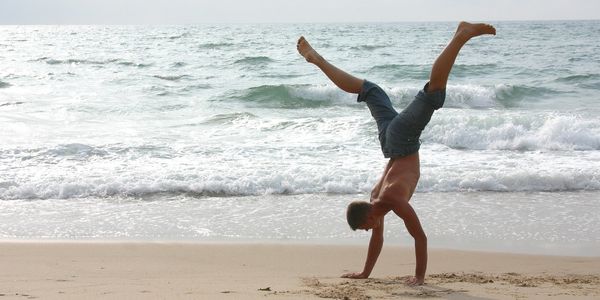 A man doing a handstand on the beach near the ocean.