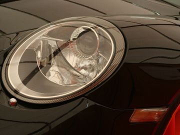 Close-up of a sleek car headlight reflecting its surroundings.