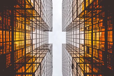 Looking up at modern glass skyscrapers with orange reflections.