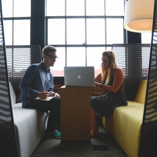 Two people collaborating on a laptop in a modern office lounge.
