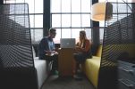 Two people having a meeting in a modern office booth with large windows.