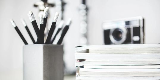 A cup holding pencils, a stack of pages and a camera... 