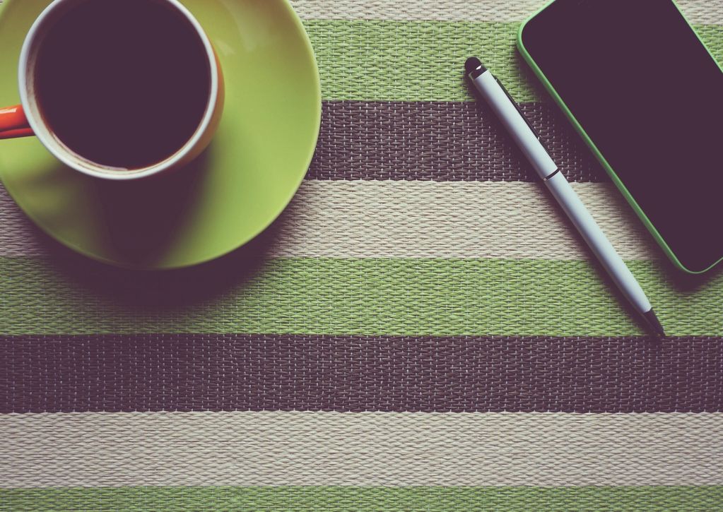 Coffee cup, pen, and phone on striped mat.