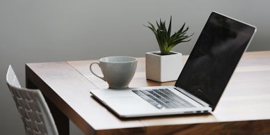 A home office with a laptop on a table, a coffee mug and a small plant on the side.