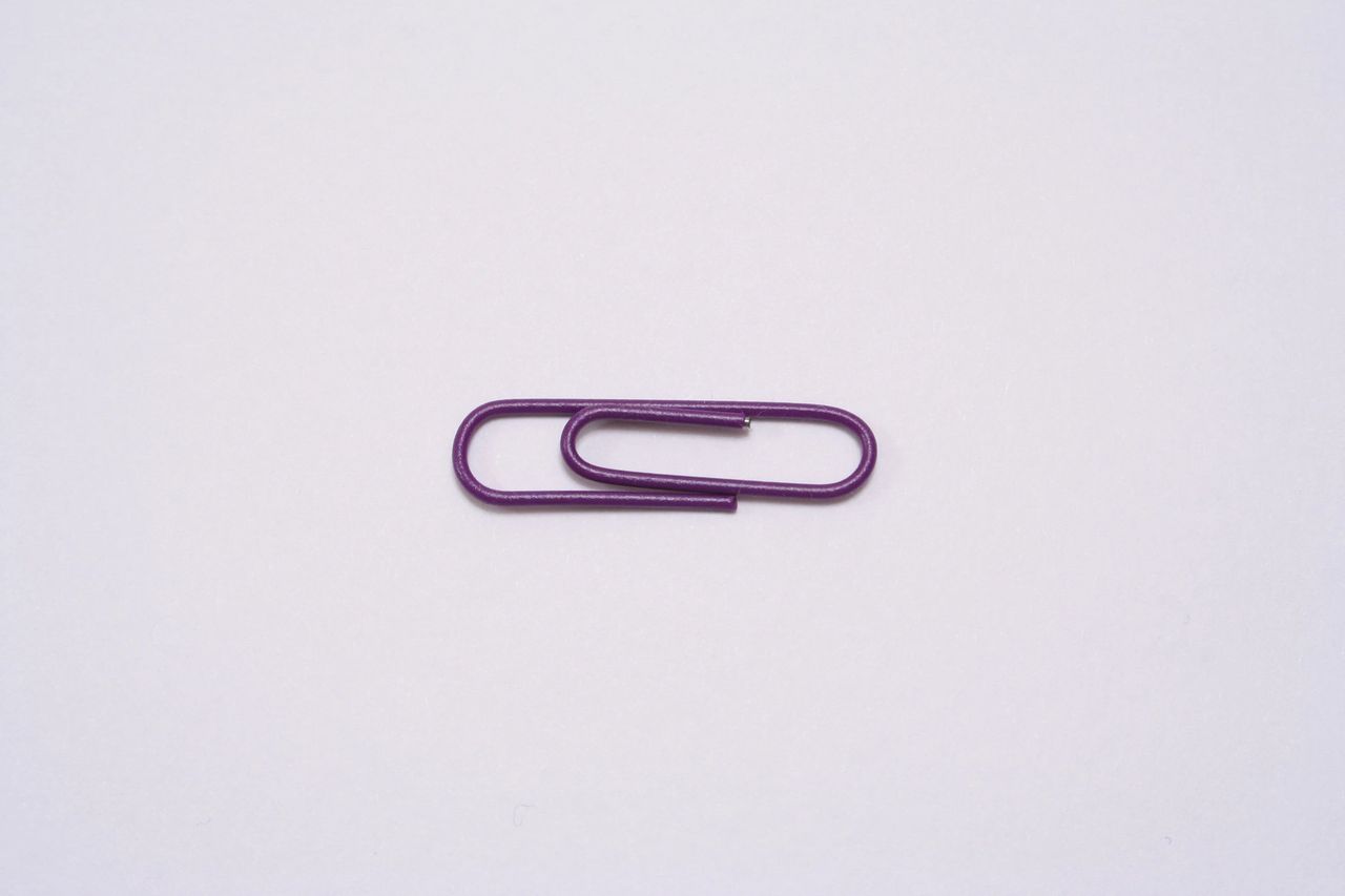 A purple paperclip sit on top of a white piece of paper.