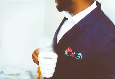 Man in a suit holding a white coffee cup with a colorful pocket square.