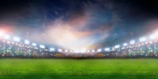 Brightly lit empty sports stadium with green field.