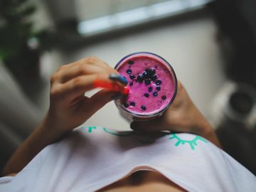 A person holding a glass with a purple smoothies with an orange straw.