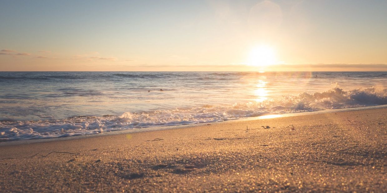 Beach at sunset. Glimmering sand and water and bright sun on horizon.