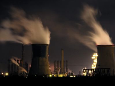 Night view of an industrial plant with smoke rising from cooling towers.