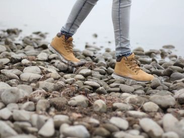 Person walking on rocky ground wearing brown boots and light jeans.