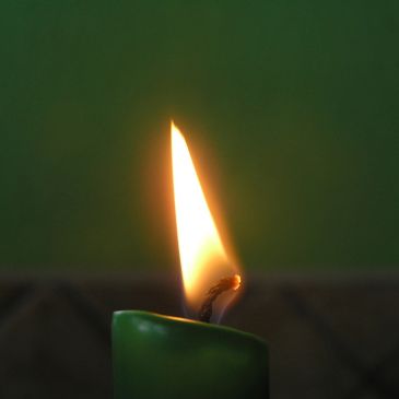 A green candle burning with a bright flame against a dark background.