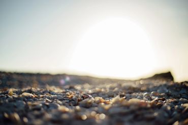Close-up of pebbles on a beach with the sun shining brightly in the background.