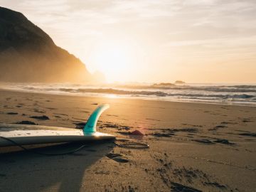 Surfboard on beach at sunset with mountains in background.
