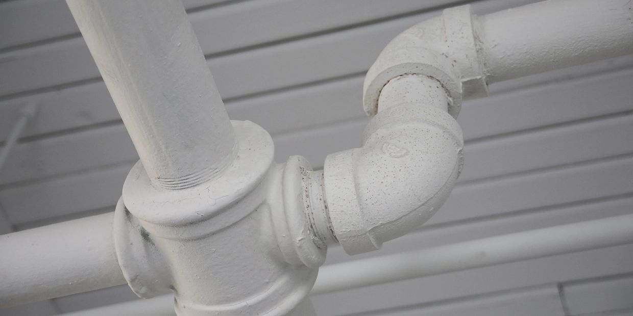 Close-up of white painted metal pipes and joints on a ceiling.