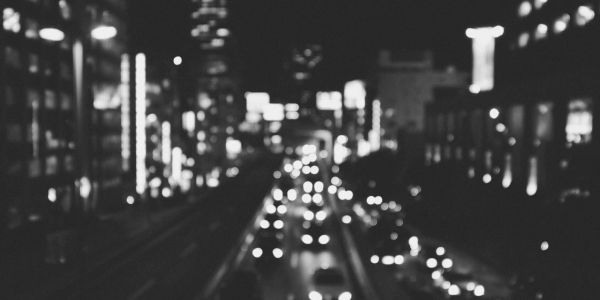 Blurry black and white city street at night with vehicle lights.